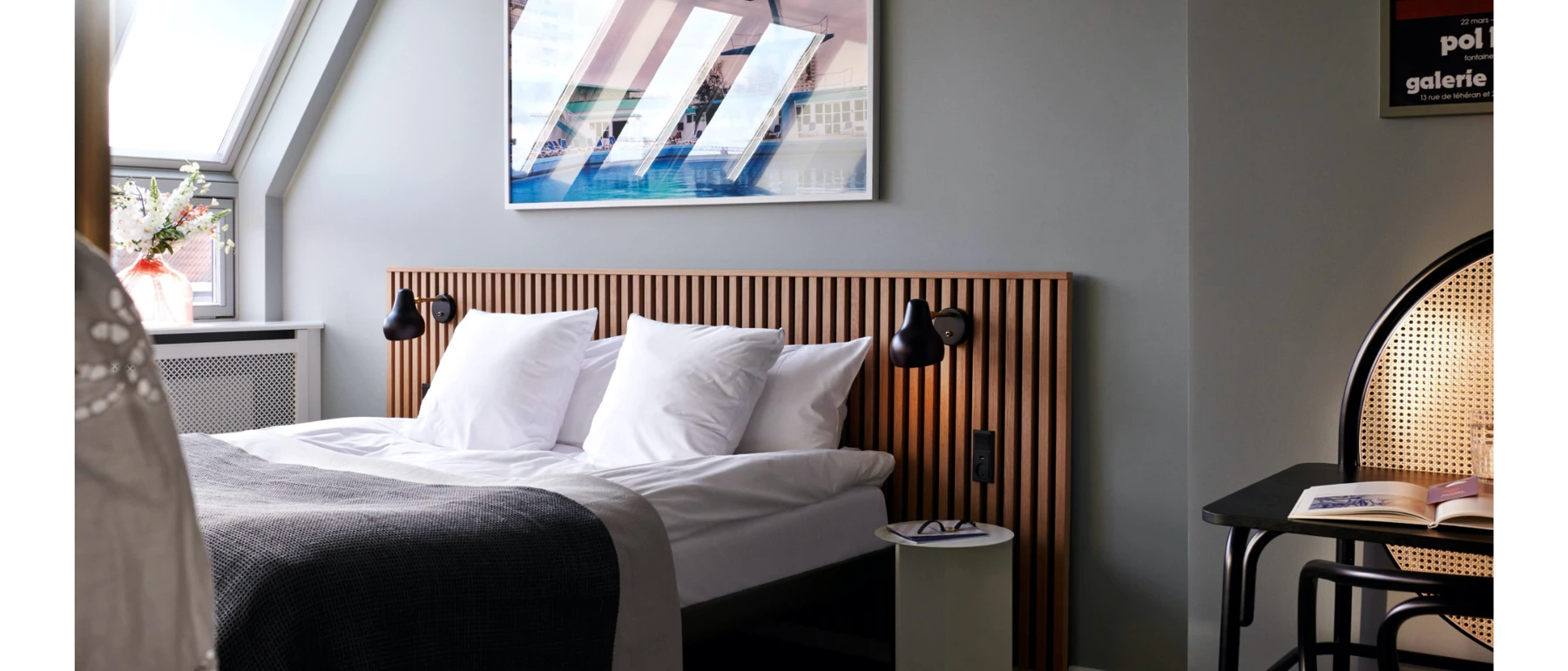 Two black AJ Wall Lamps flank a bed in a bright hotel room with a slatted wooden headboard. © 2026 Louis Poulsen.