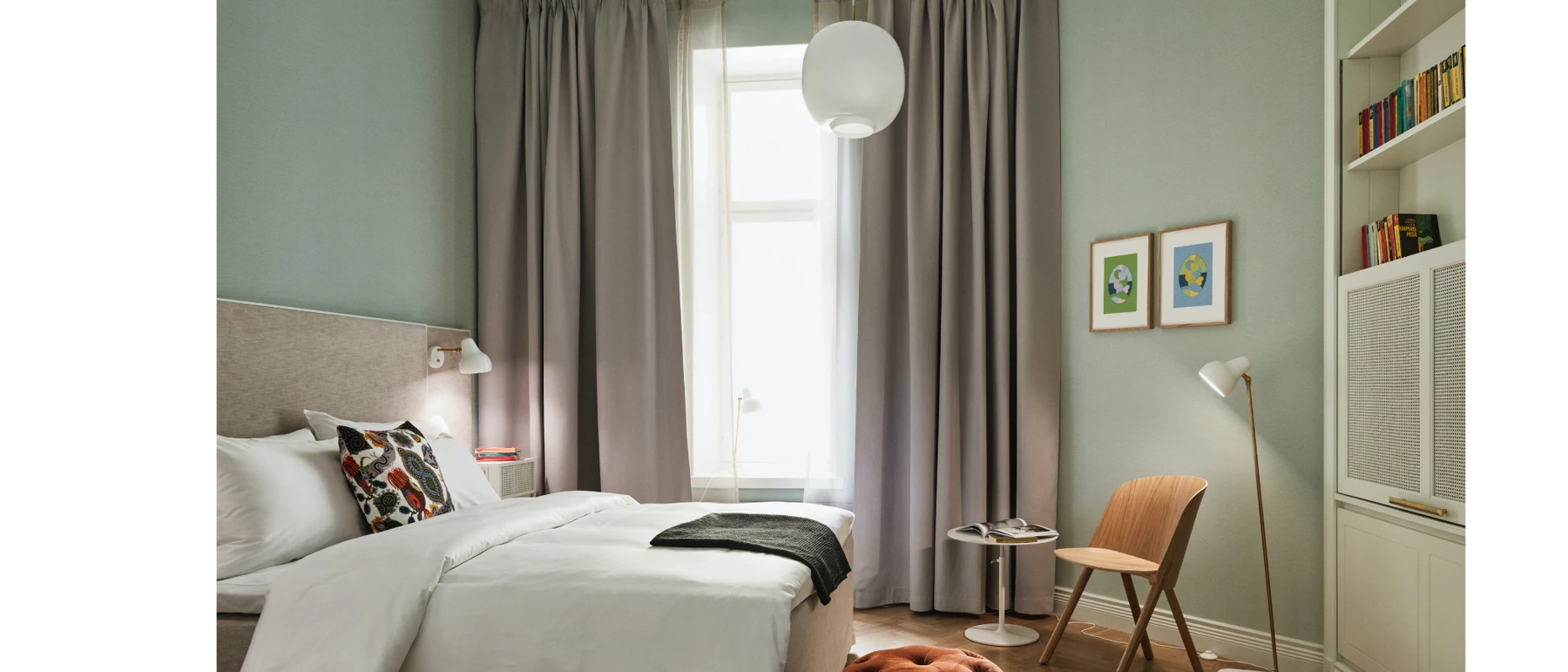 A VL 45 Radiohus Pendant, AJ Wall Lamp and AJ Floor Lamp in a bright hotel room with pale green walls. © 2026 Louis Poulsen.