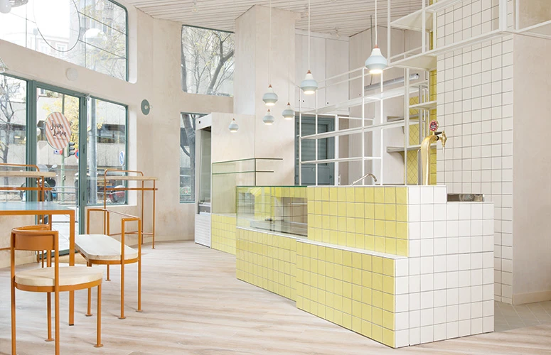 Toldbod pendler hænger over disken i Juana Limón Café med gule og hvide fliser og store vinduer. © 2026 Louis Poulsen.