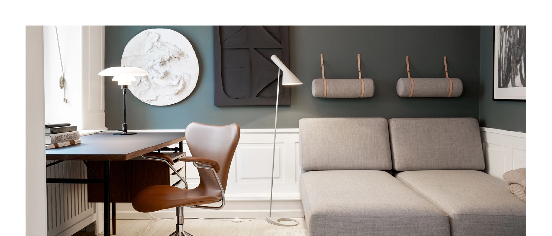 A PH 3/2 Table Lamp and an AJ Floor Lamp stand beside a desk and sofa in a dark green room. © 2026 Louis Poulsen.