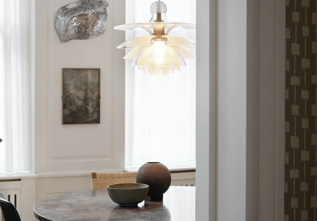 A PH Septima pendant in opal-white glass glows above a round marble table in a bright dining room. © 2026 Louis Poulsen.