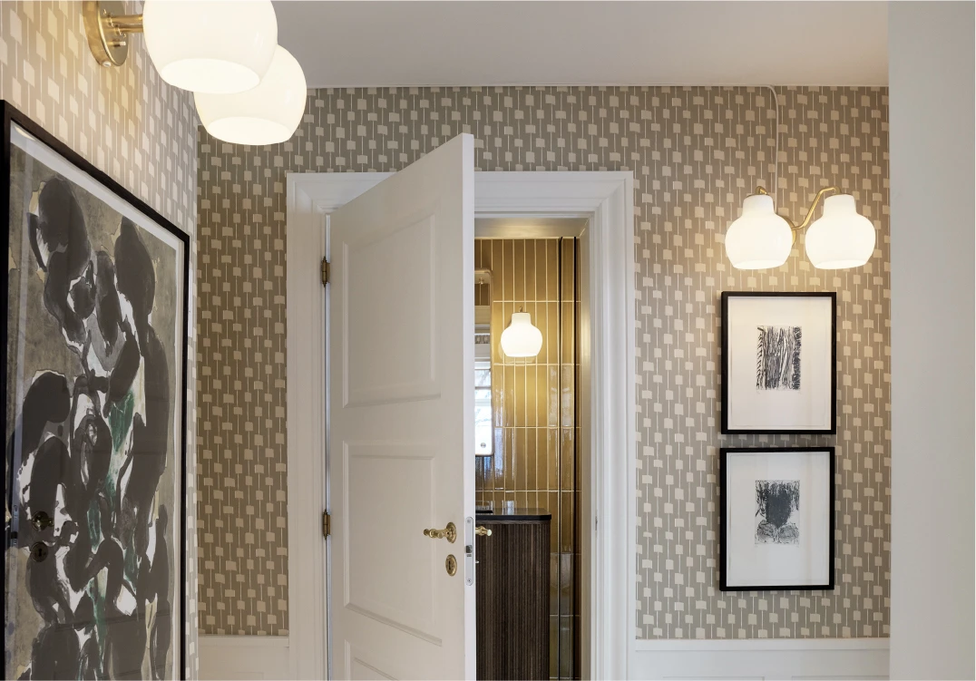 VL Ring Crown 2 Wall Lamps in brass with opal glass shades light a patterned hallway at The Darling. © 2026 Louis Poulsen.