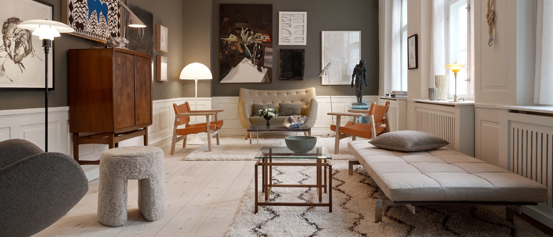 A PH 80 floor lamp and Panthella 320 Table Lamp in a bright living room with artwork, wooden furniture and large windows. © 2026 Louis Poulsen.