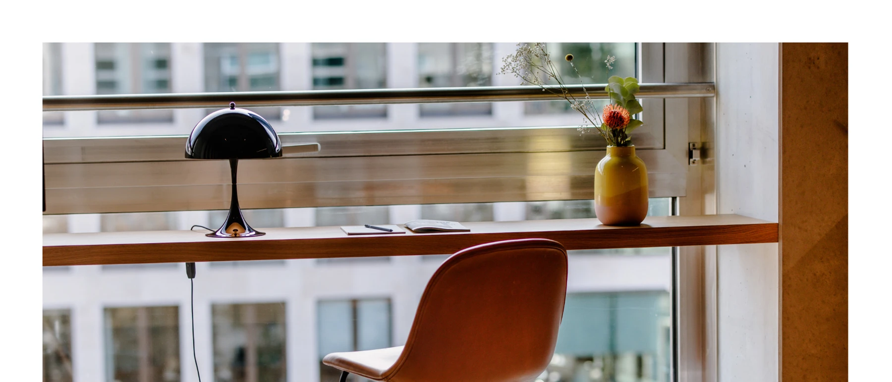 A black Panthella 250 Table Lamp sits on a wooden window ledge beside a leather chair. © 2026 Louis Poulsen.