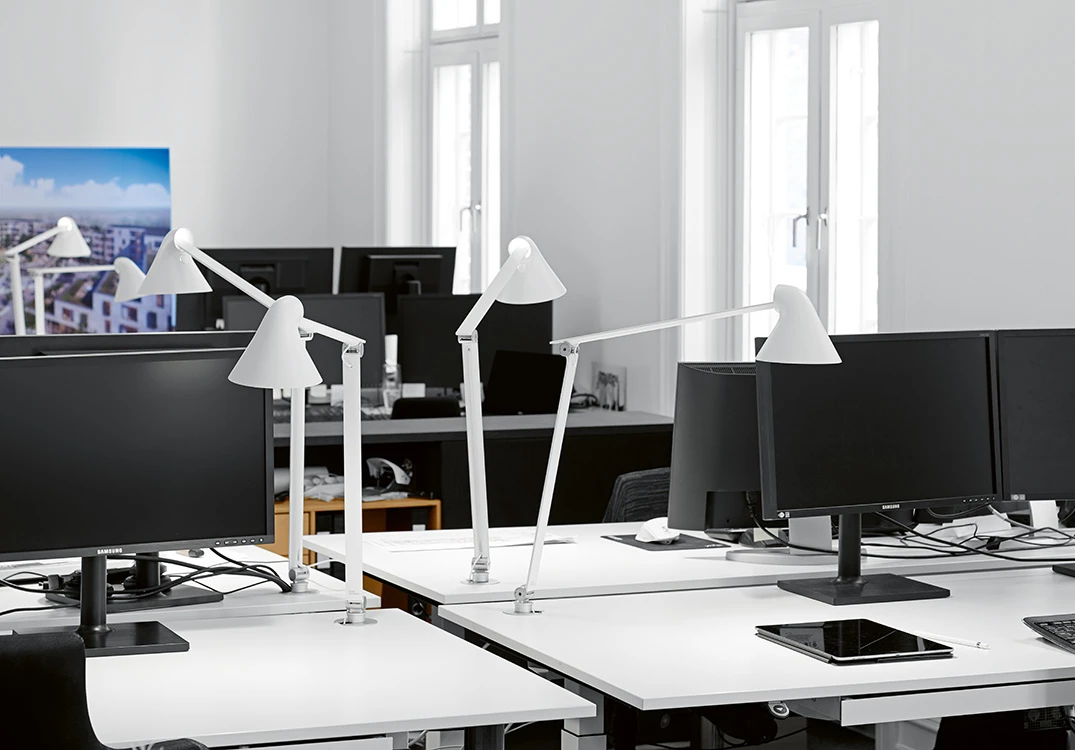 White NJP Table Lamps on desks in a bright office with computer monitors. © 2026 Louis Poulsen.
