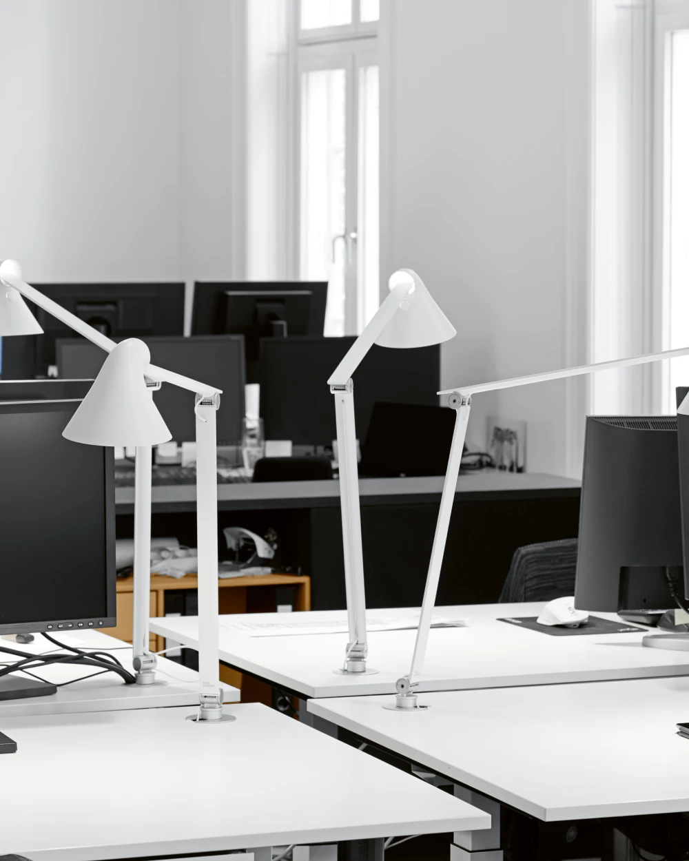 Witte NJP tafellampen staan op bureaus in een licht, modern kantoor met computerschermen. © 2026 Louis Poulsen.
