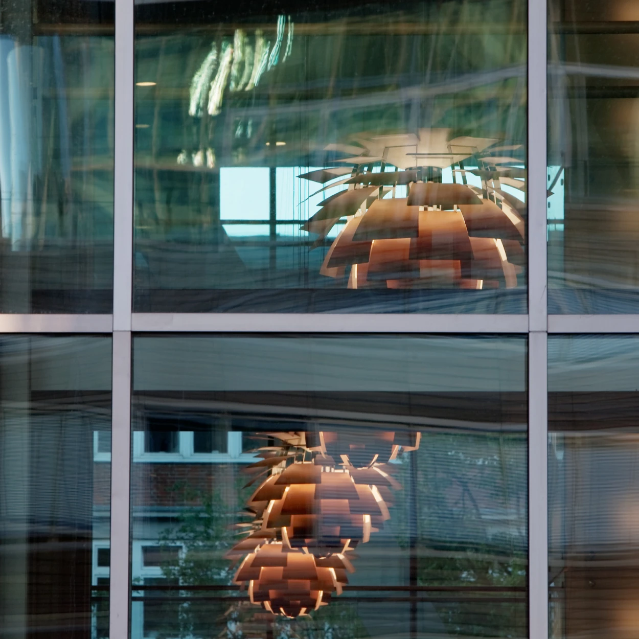 Koperkleurige PH Artichoke hanglampen geven warm licht in een kantoor, gezien door de glazen gevel. © 2026 Louis Poulsen.