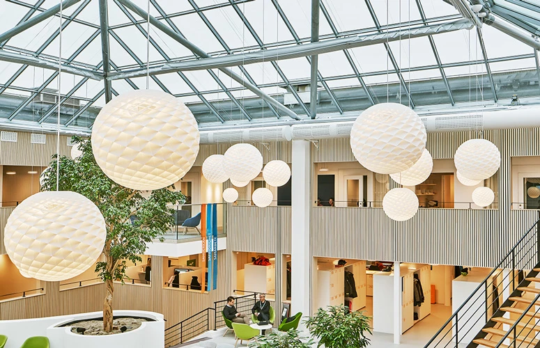 White Patera Pendants hang beneath the glass roof of the Kraftringen office atrium in Lund. © 2026 Louis Poulsen.