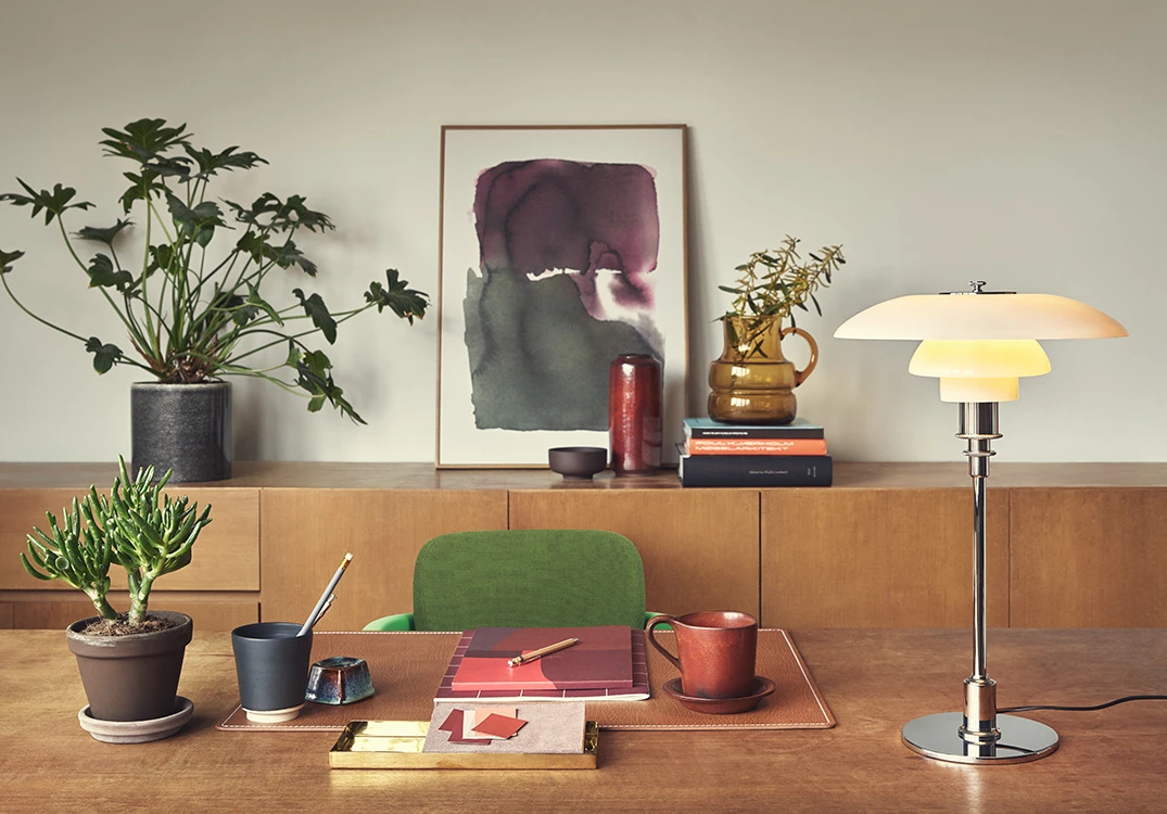 A PH 3/2 Table Lamp in opal glass and chrome stands on a desk in a warmly furnished office. © 2026 Louis Poulsen.
