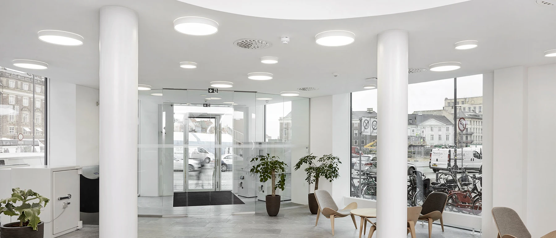LP Circle Surface Mounted ceiling lights evenly illuminate Sydbank’s bright foyer, with its glass façade and seating area. © 2026 Louis Poulsen.
