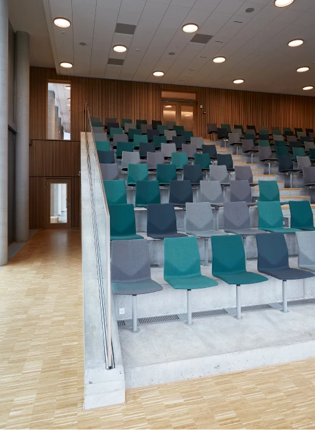 LP Slim Round inbouwspots verlichten een auditorium met rijen turkooizen en grijze stoelen. © 2026 Louis Poulsen.