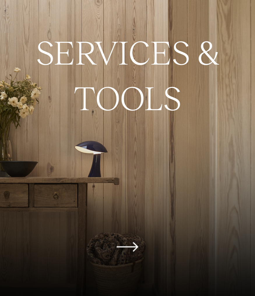 Services & Tools – een donkere Panthella 160 Portable Lamp op een houten tafel in een kamer met houten wandpanelen. © 2026 Louis Poulsen.