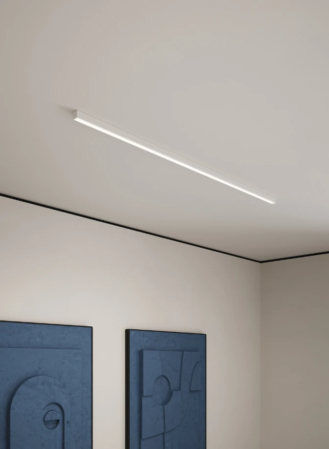 A white LP LIN25 Surface ceiling light forms a slim line across the ceiling above blue artwork in a modern room. © 2026 Louis Poulsen.