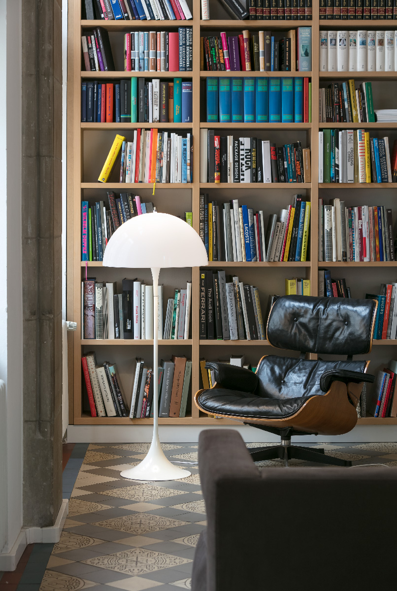 A white Panthella Floor Lamp stands in front of a bookcase beside a leather lounge chair. © 2026 Louis Poulsen.