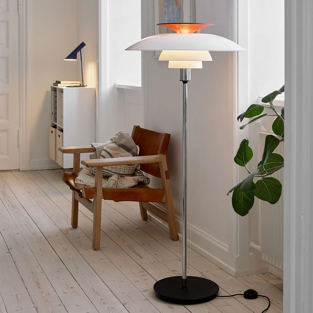En vit PH 80 golvlampa med kromad stång lyser upp en läderfåtölj i ett ljust rum med ljusa trägolv. © 2026 Louis Poulsen.