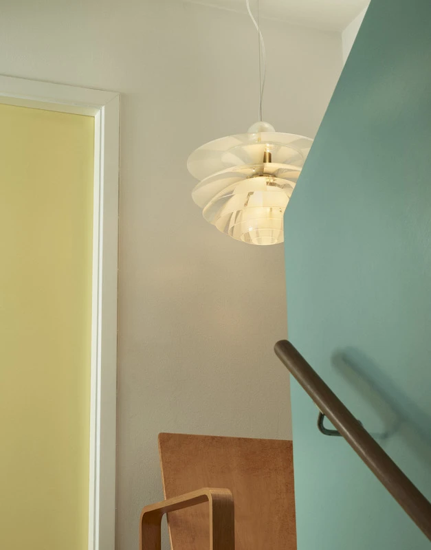 An illuminated PH Septima pendant hangs above a staircase with a turquoise wall and wooden handrail. © 2026 Louis Poulsen.