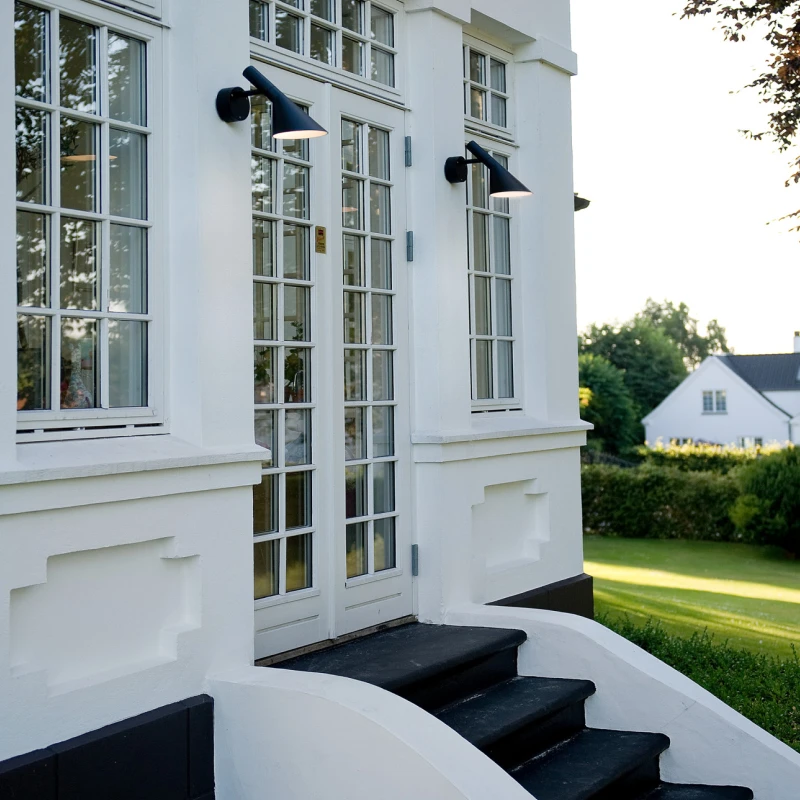 Two black AJ 50 Outdoor Wall Lamps illuminate the white facade beside the entrance. © 2026 Louis Poulsen.