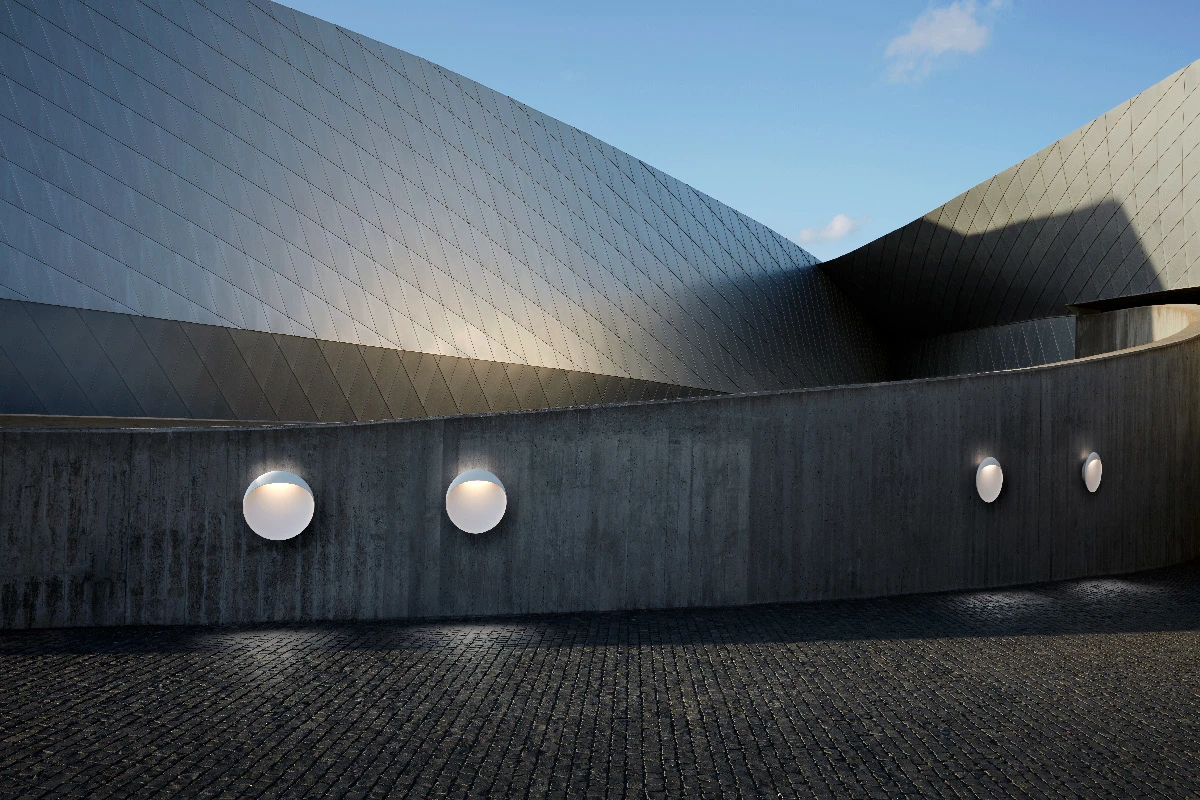 Witte Flindt-wandlampen verlichten een gebogen betonnen muur bij een modern gebouw. © 2026 Louis Poulsen.