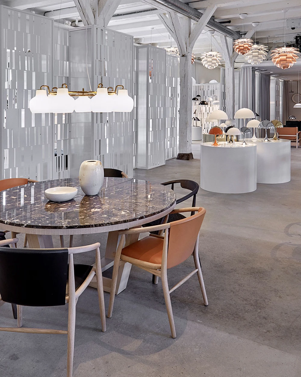 White and copper PH Artichoke pendants hang above a showroom with display tables, chairs and table lamps. © 2026 Louis Poulsen.