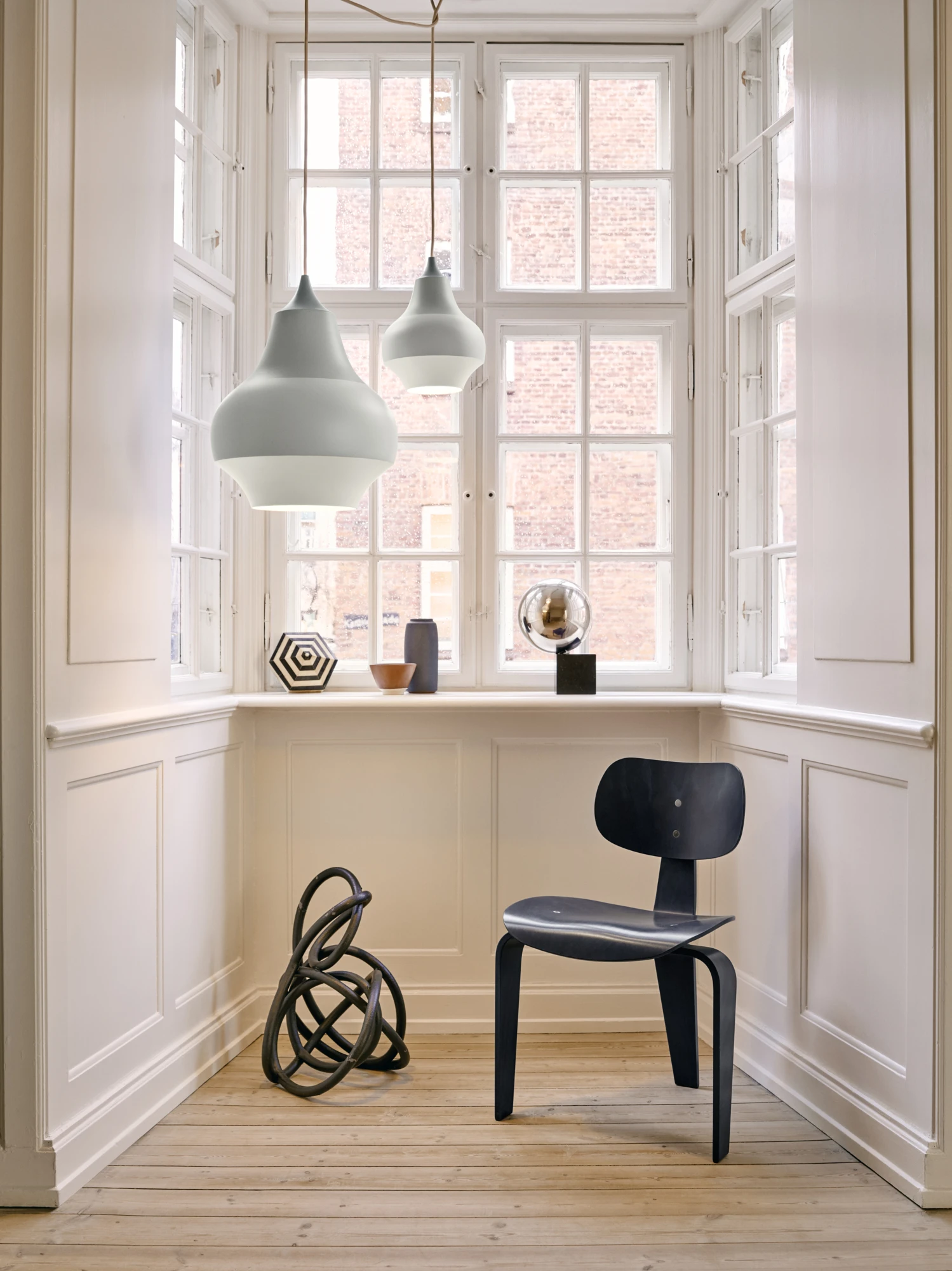 Two white Cirque Pendants hang in front of tall windows in a bright room with classic wall panelling. © 2026 Louis Poulsen.