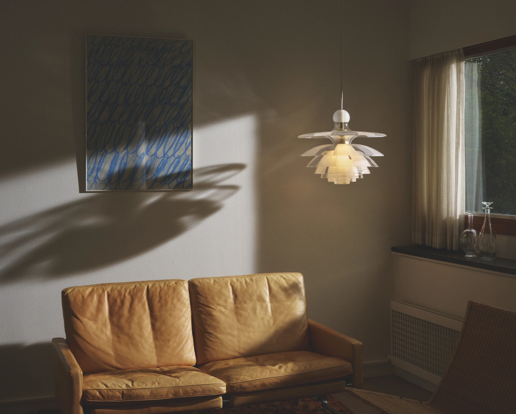 PH Septima hanglamp met gelaagde glazen kappen boven een bruine leren bank in een zonnige woonkamer. © 2026 Louis Poulsen.