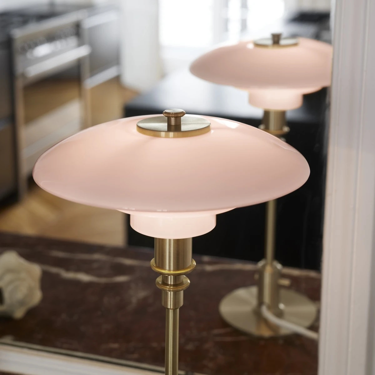 Two PH 2/2 Question Mark Pale Rose Table Lamps with pale rose glass shades and brass stems stand on a marble table. © 2026 Louis Poulsen.
