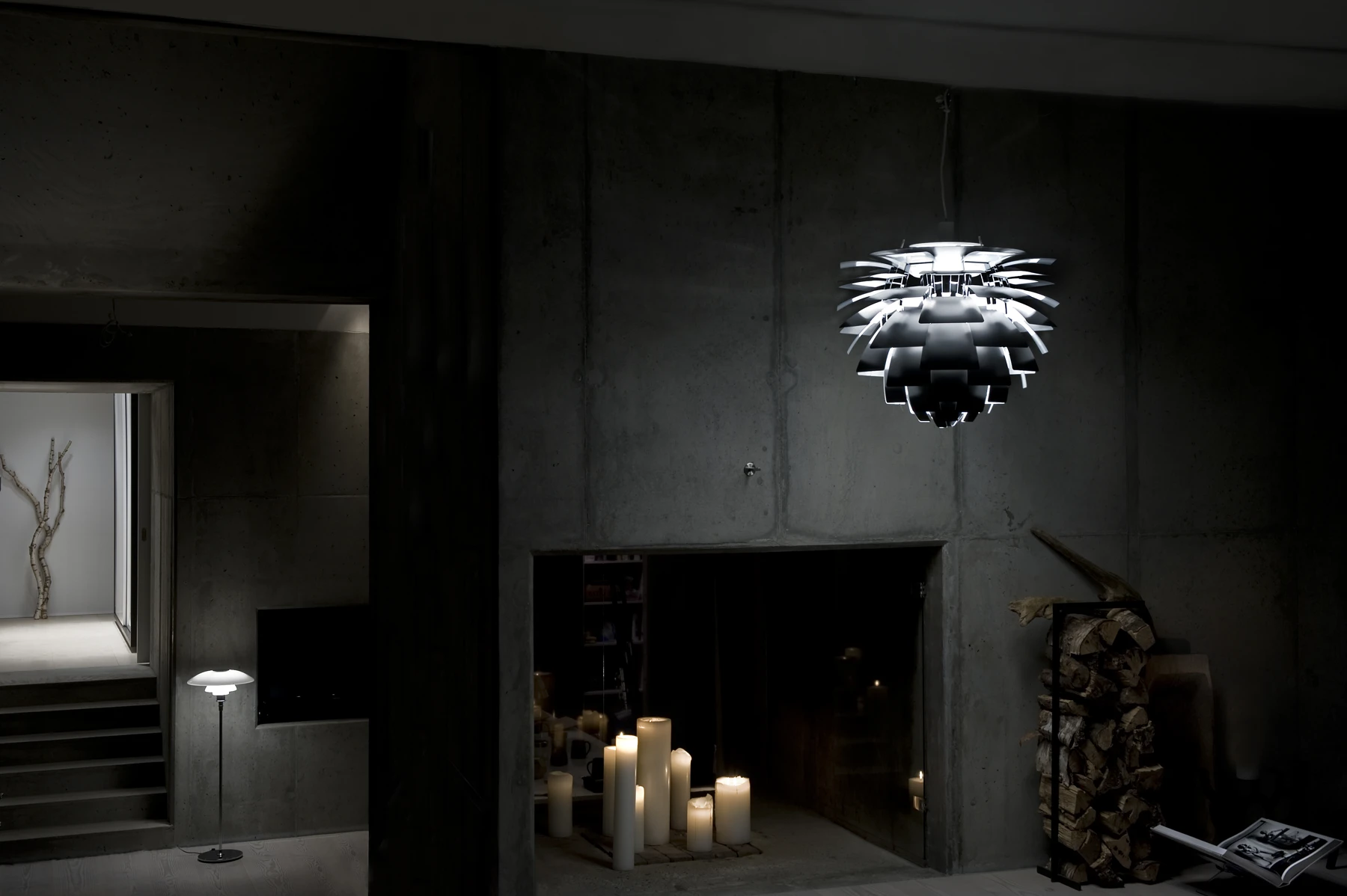 A black PH Artichoke pendant illuminates candles in a dim room with raw concrete walls. © 2026 Louis Poulsen.