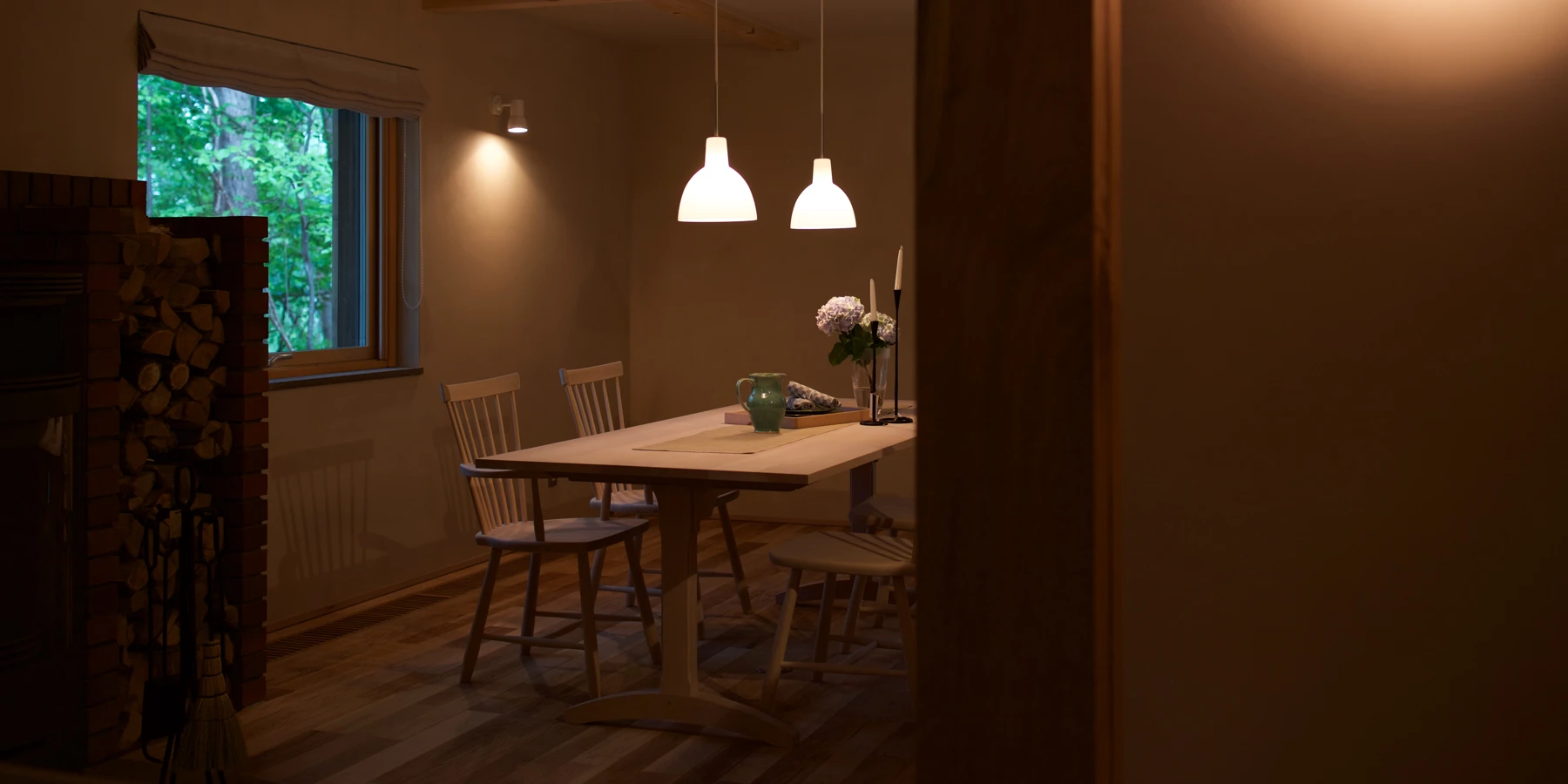 Two white Toldbod Pendant lights hang above a wooden dining table in a warmly lit room. © 2026 Louis Poulsen.