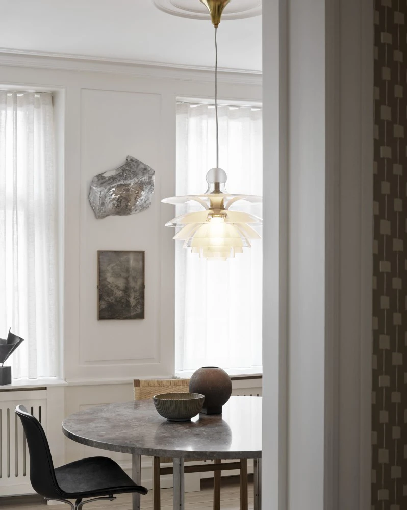 A PH Septima pendant in opal white hangs above a round dining table in a bright dining room. © 2026 Louis Poulsen.
