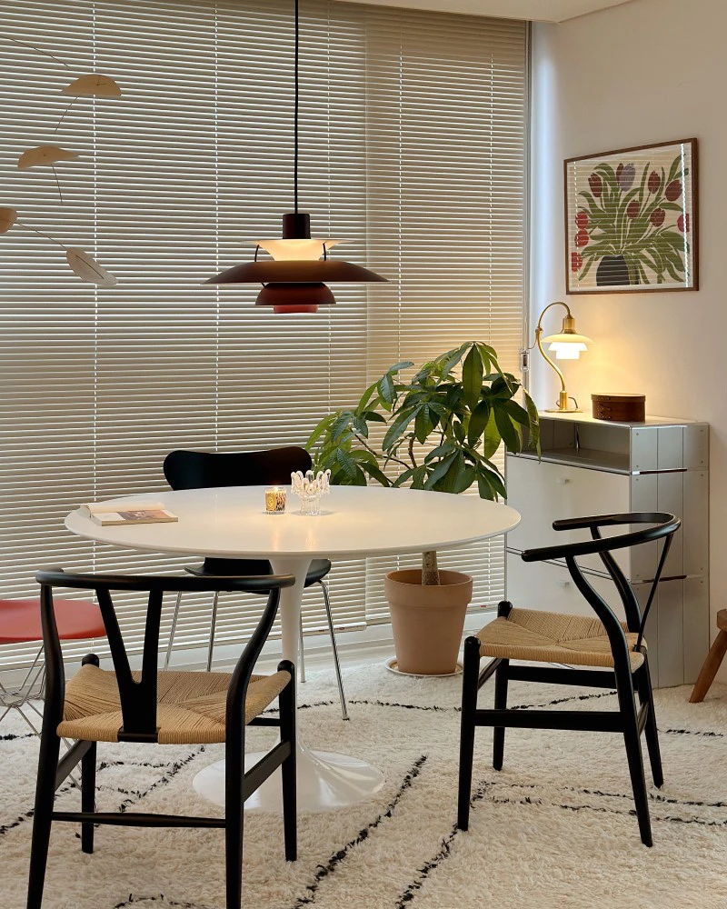 A burgundy PH 5 pendant hangs above a round dining table surrounded by black wooden chairs in a bright room. © 2026 Louis Poulsen.