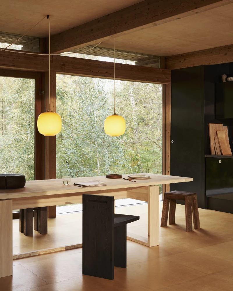 Two VL 45 Radiohus Pendants in brass with glossy pale yellow glass hang above a dining table in a timber home. © 2026 Louis Poulsen.