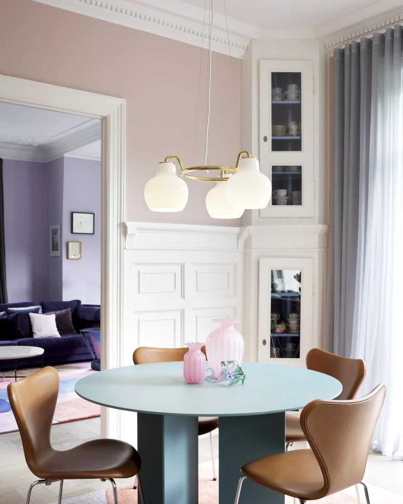 A brass VL Ring Crown 3-5-7 Pendant with opal-white shades hangs above a round dining table in a bright room. © 2026 Louis Poulsen.