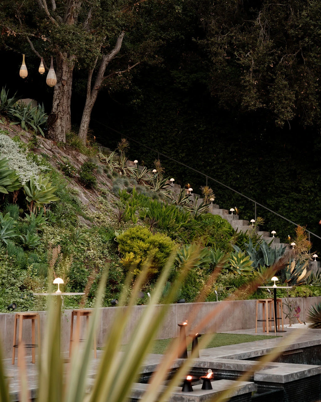 Panthella 160 Portable Lamps with white shades illuminate steps in a lush garden beside a pool. © 2026 Louis Poulsen.