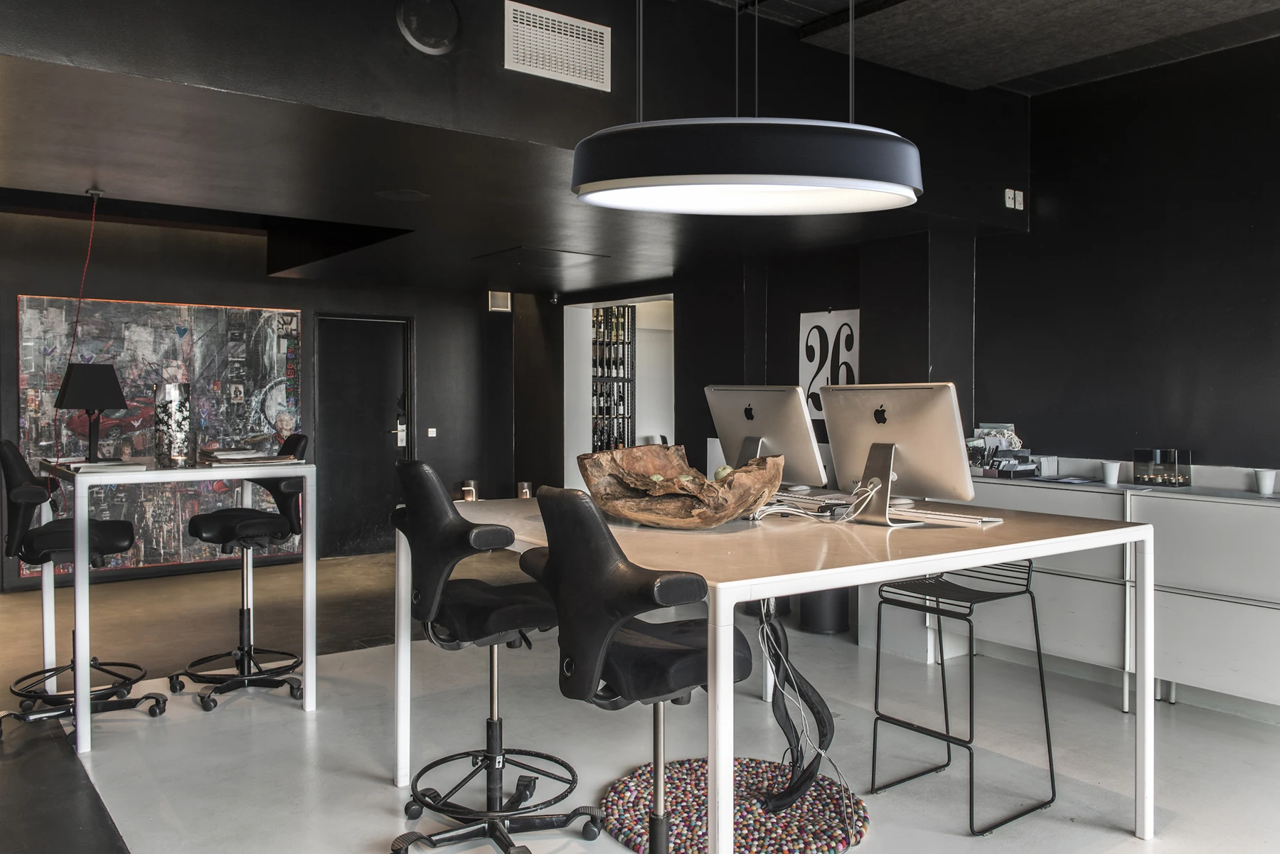 A black LP Grand Suspended illuminates a large worktable in a dark office. © 2026 Louis Poulsen.