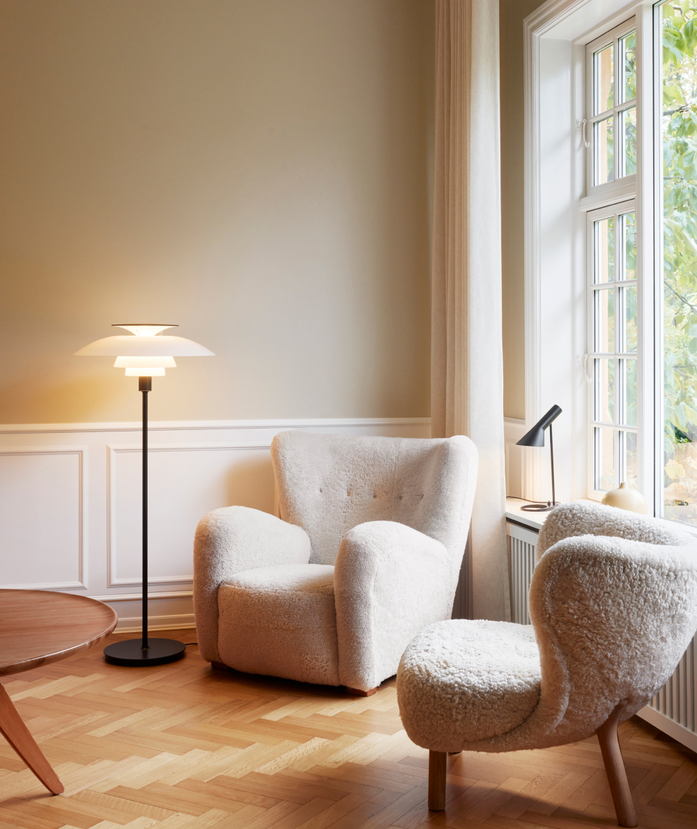 A PH 80 Floor Lamp and a black AJ Table Lamp stand beside soft armchairs in a bright living room. © 2026 Louis Poulsen.