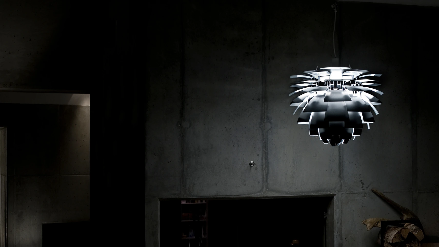 A silver PH Artichoke pendant glows against a dark, raw concrete wall. © 2026 Louis Poulsen.