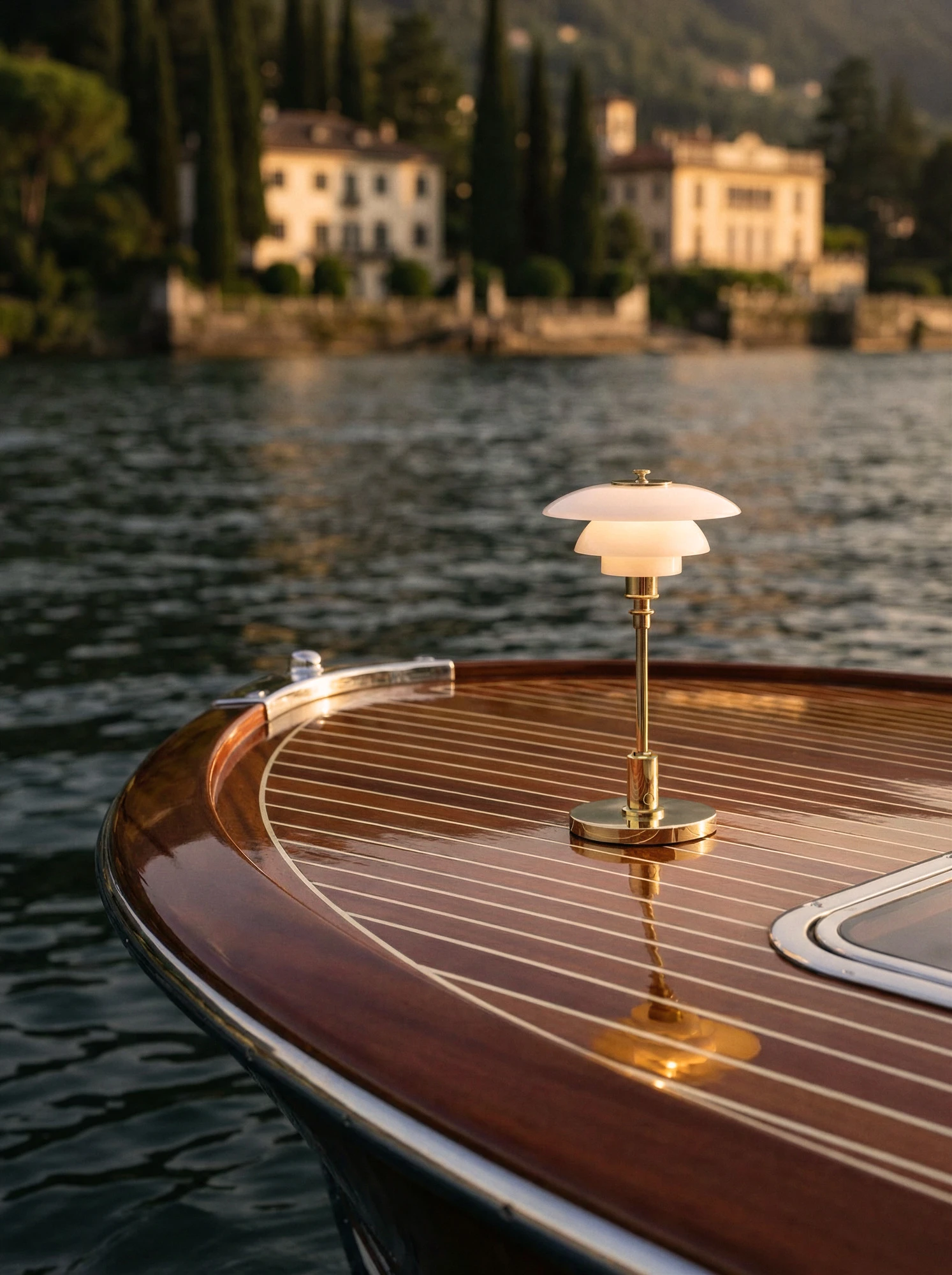 La lampe portable PH 1/1 en laiton éclaire le pont en bois d’un bateau au bord de l’eau. © 2026 Louis Poulsen.