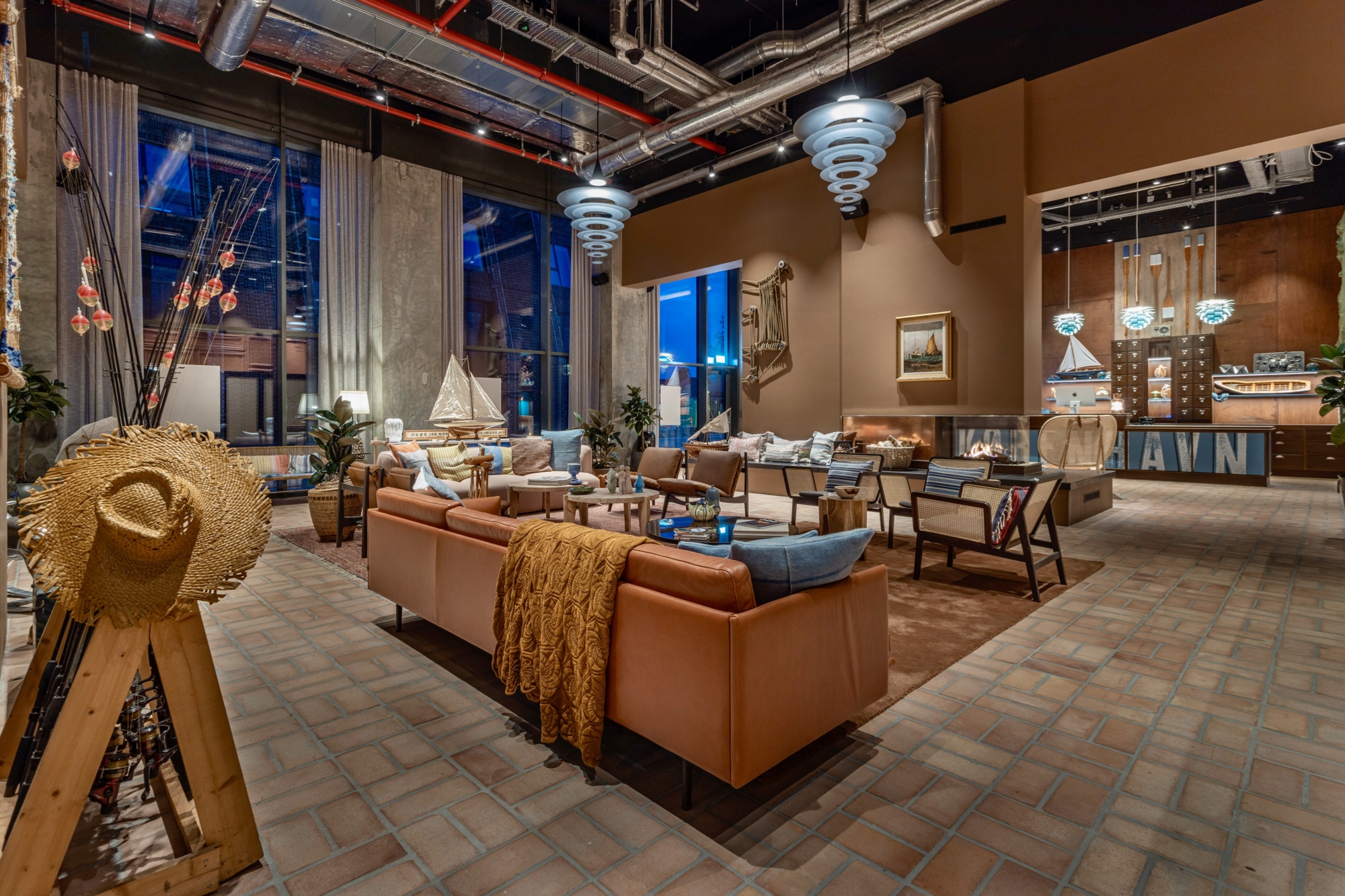 Enigma Pendants hang over the 25hours Hotel lounge, with armchairs, sofas and exposed ceiling pipes. © 2026 Louis Poulsen.