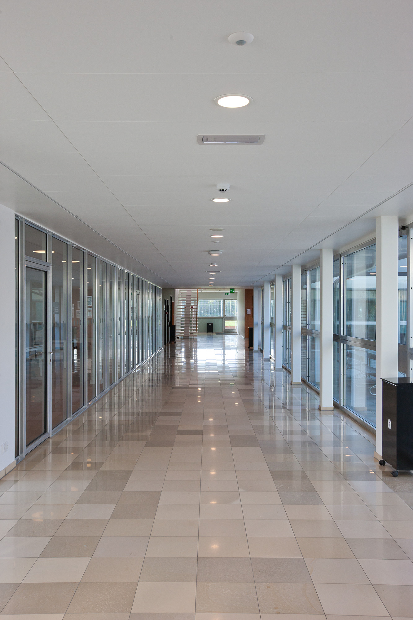 Round recessed ceiling lights illuminate a long, tiled corridor at Aarhus Statsgymnasium. © 2026 Louis Poulsen.