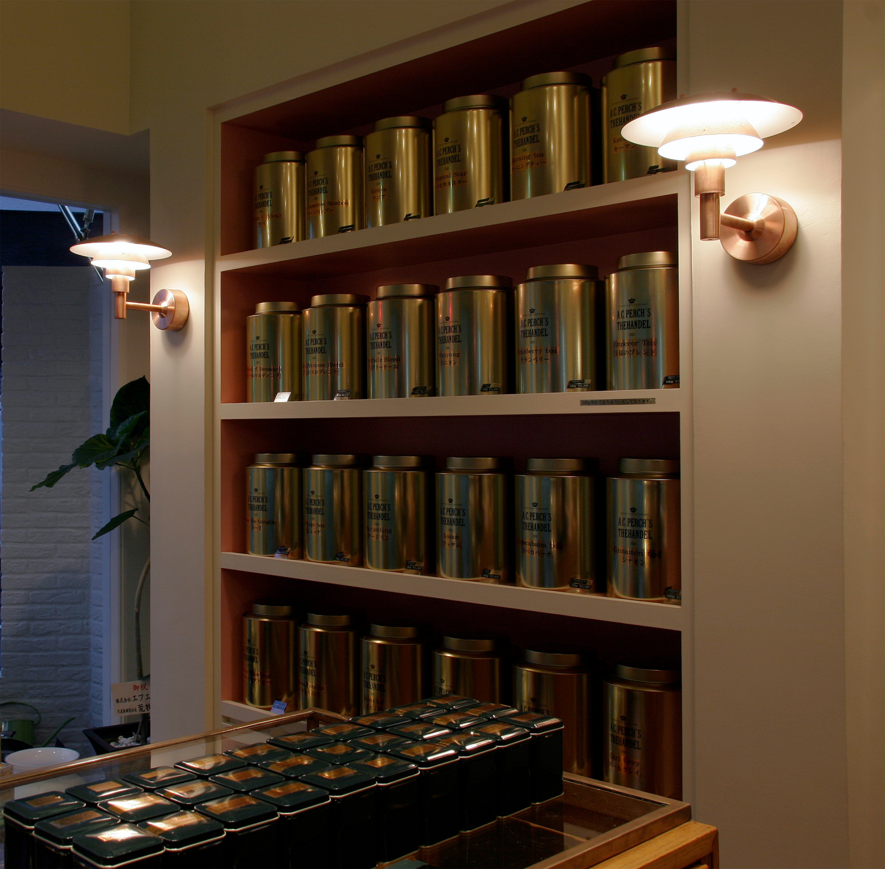 PH 2/1 Wall Lamps with white shades illuminate a Japanese tea shop lined with shelves of tea tins. © 2026 Louis Poulsen.