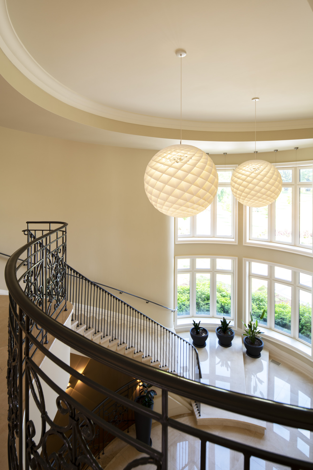 Two white Patera Pendants hang in a bright atrium with curved windows and a sweeping staircase. © 2026 Louis Poulsen.