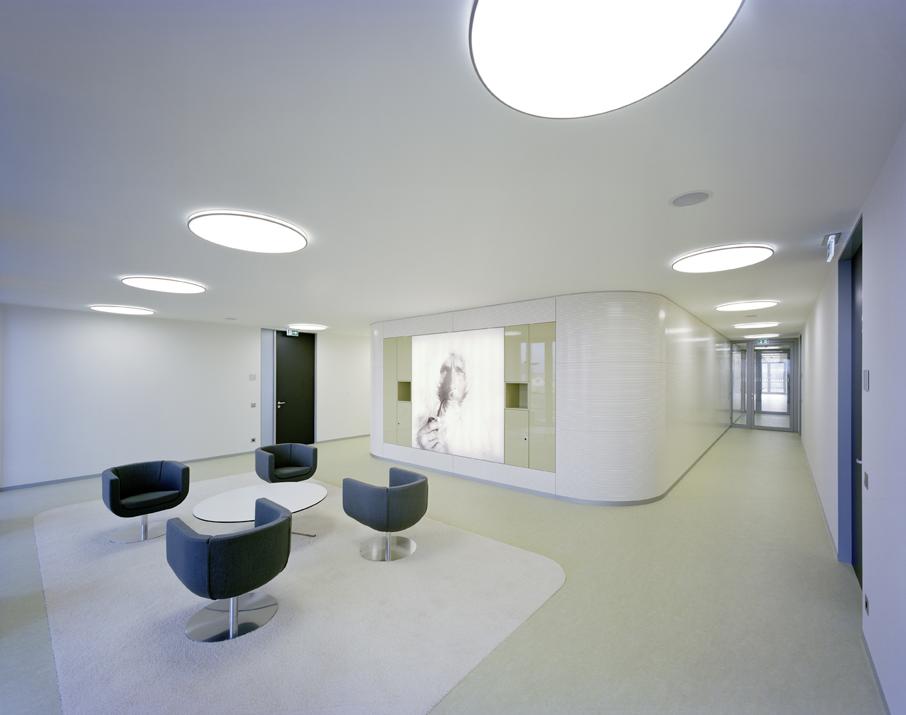 AJ Munkegaard Ceiling Lamps illuminate a bright institutional lobby with dark lounge chairs and a long corridor. © 2026 Louis Poulsen.