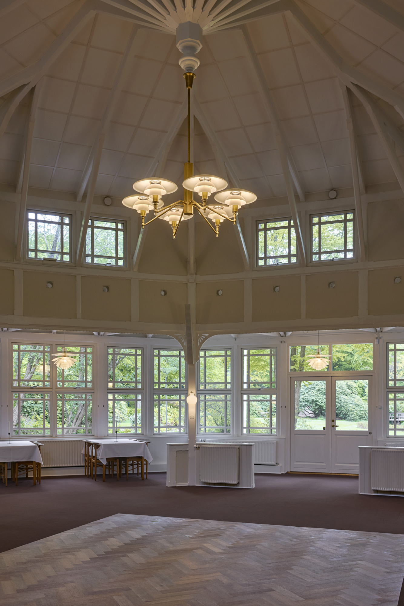 A PH 3/2 Academy chandelier lights the high pavilion, with PH Septima pendants and a VL Ring Crown 1 Wall Lamp. © 2026 Louis Poulsen.