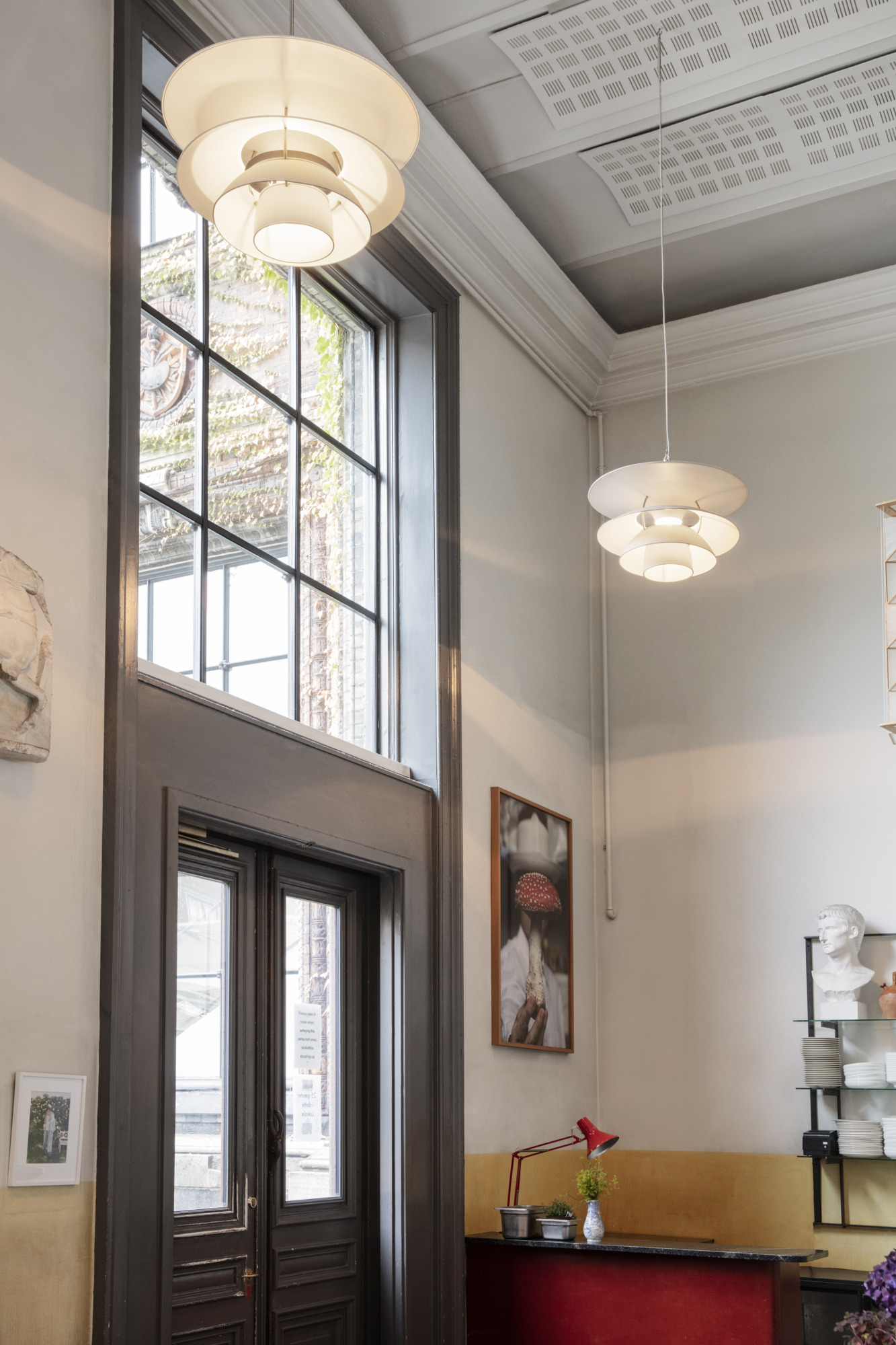 Two white PH 5-4½ & PH 6½-6 pendants illuminate the Apollo Bar beside its tall windows. © 2026 Louis Poulsen.