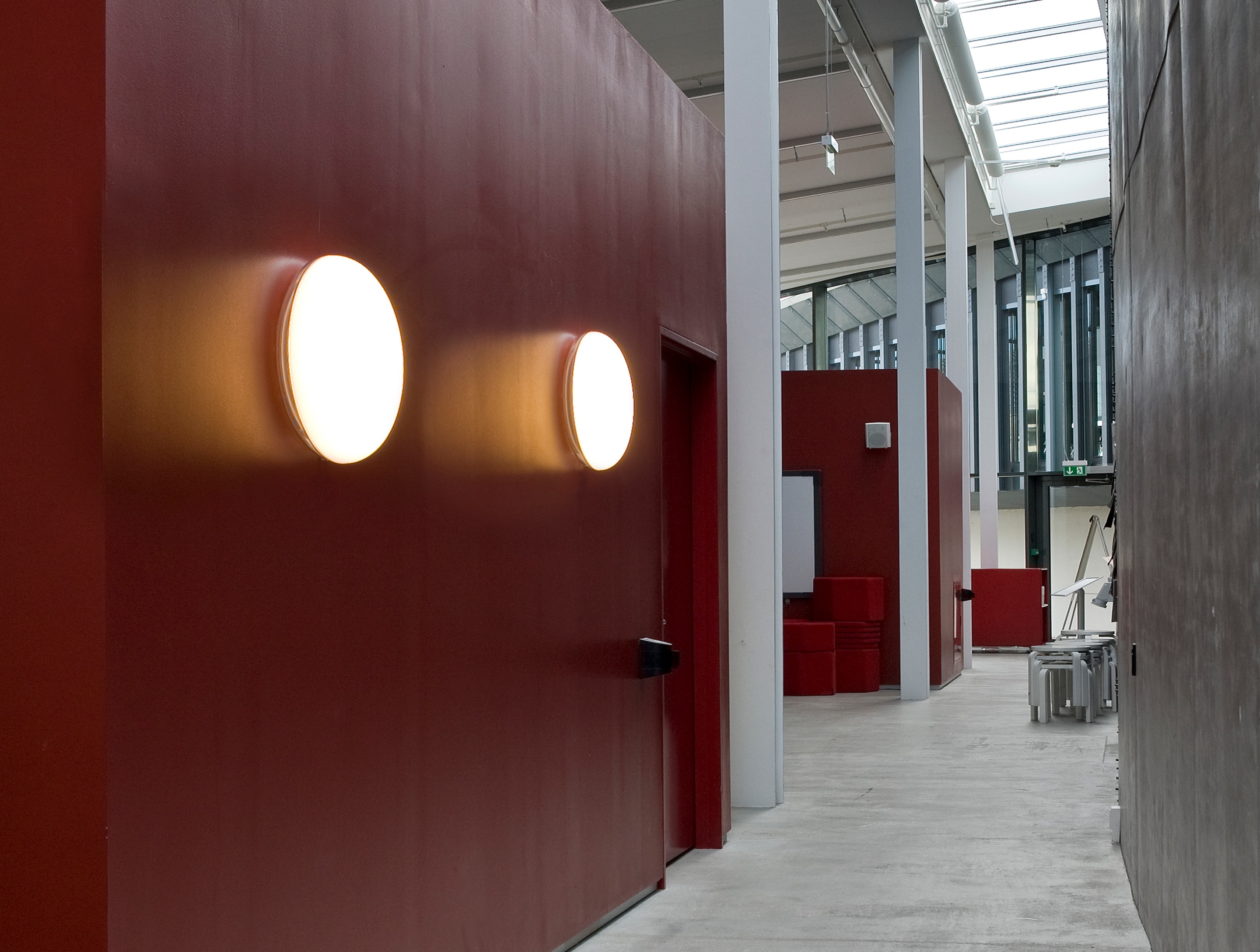Silverback Ceiling/Wall Lamps cast a warm glow on a red wall in a bright Arken corridor. © 2026 Louis Poulsen.