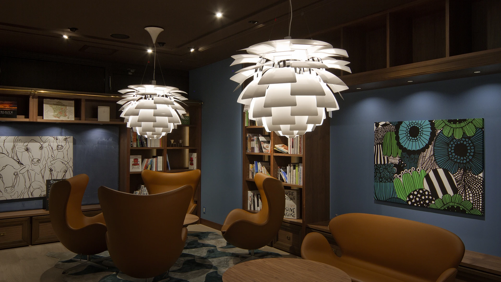 Two white PH Artichoke pendants illuminate armchairs in a dark library with bookshelves and artwork. © 2026 Louis Poulsen.