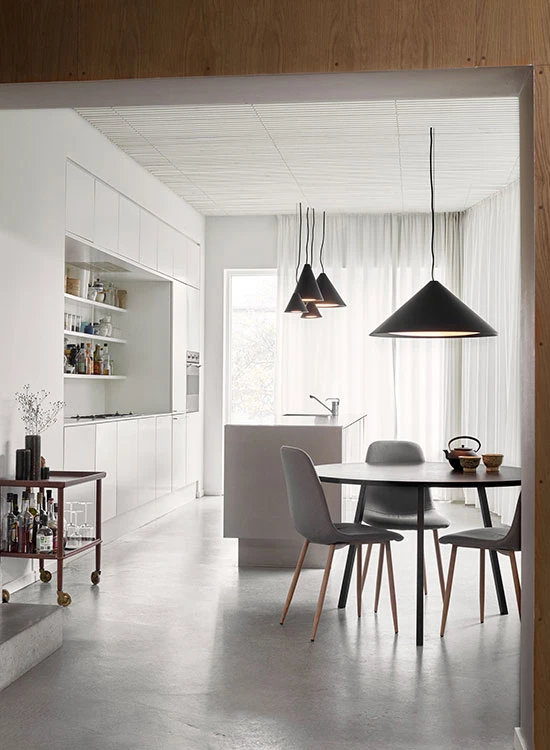 Svarte Keglen-pendler i ulike størrelser henger over spisebordet i et lyst, moderne kjøkken. © 2026 Louis Poulsen.