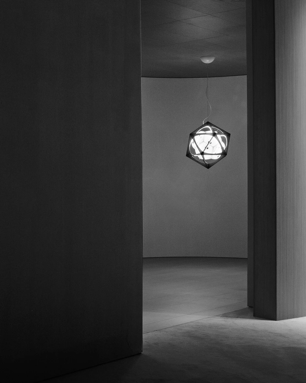 OE Quasi Light-pendlen lyser i et minimalistisk rum med glatte vægge og gulv i sort-hvidt. © 2026 Louis Poulsen.