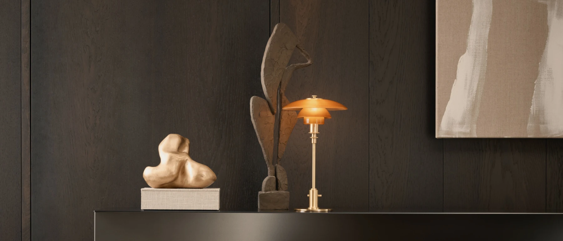 PH 2/1 Pale Rose Brass bordlampe med varmt roséguldsskær på en mørk hylde ved skulpturer. © 2026 Louis Poulsen.